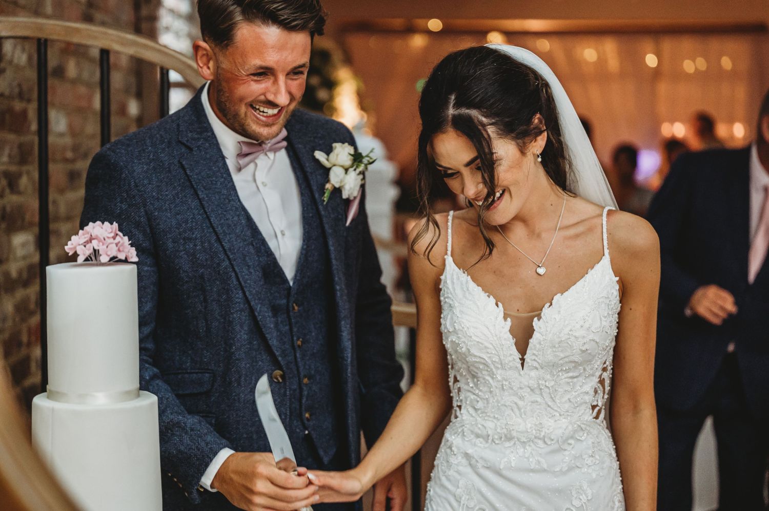 A wedding couple stands beside their elegant white wedding cake during their reception.