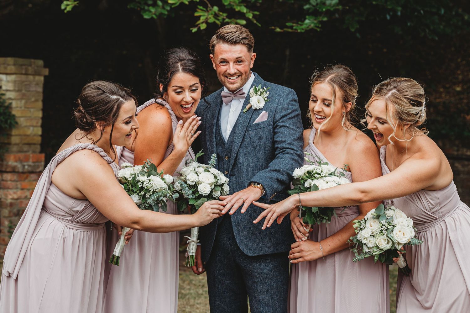 Bridesmaids in blush dresses react excitedly to seeing wedding ring.