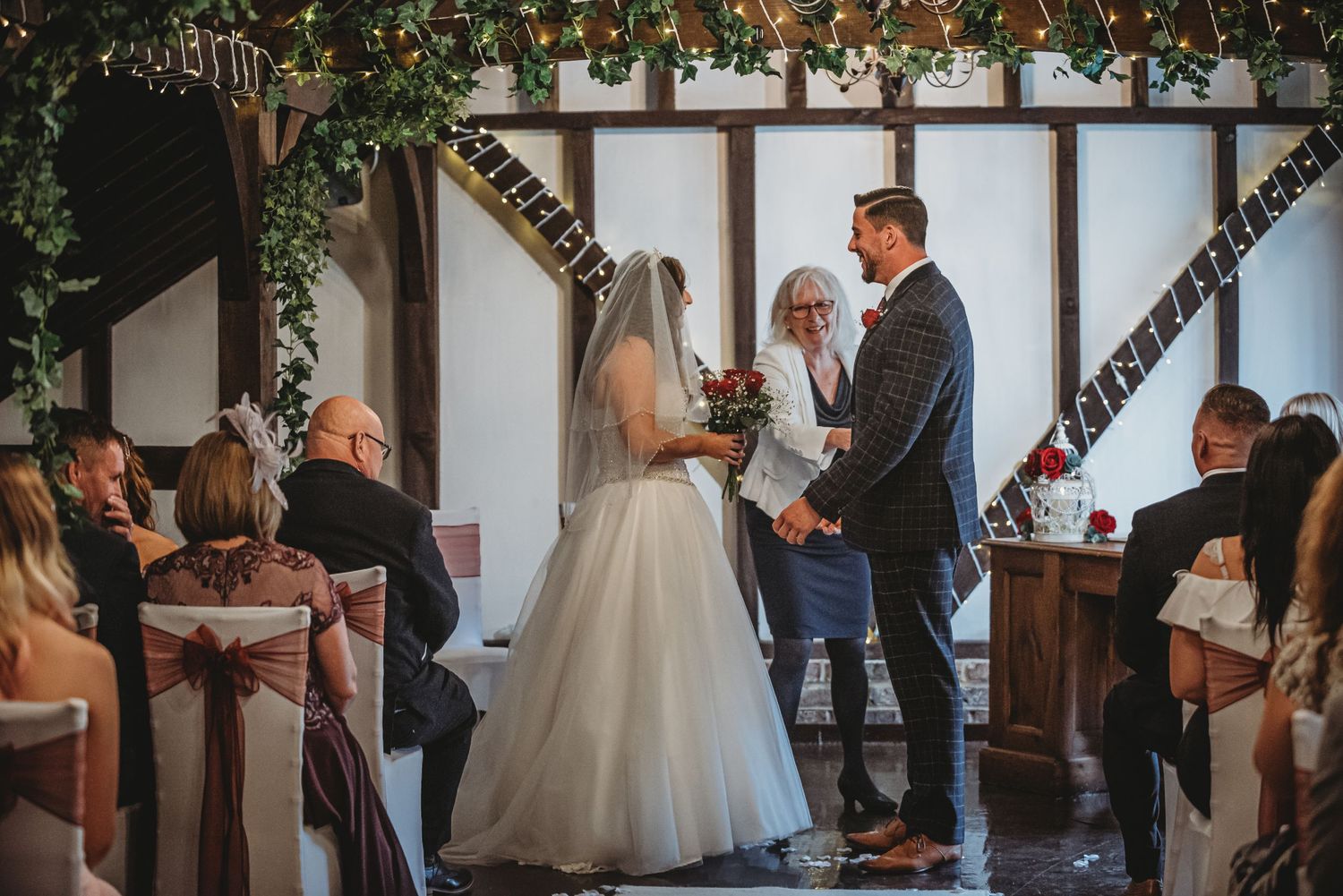 Wedding ceremony in a rustic venue with wooden cross beams and floral decorations.