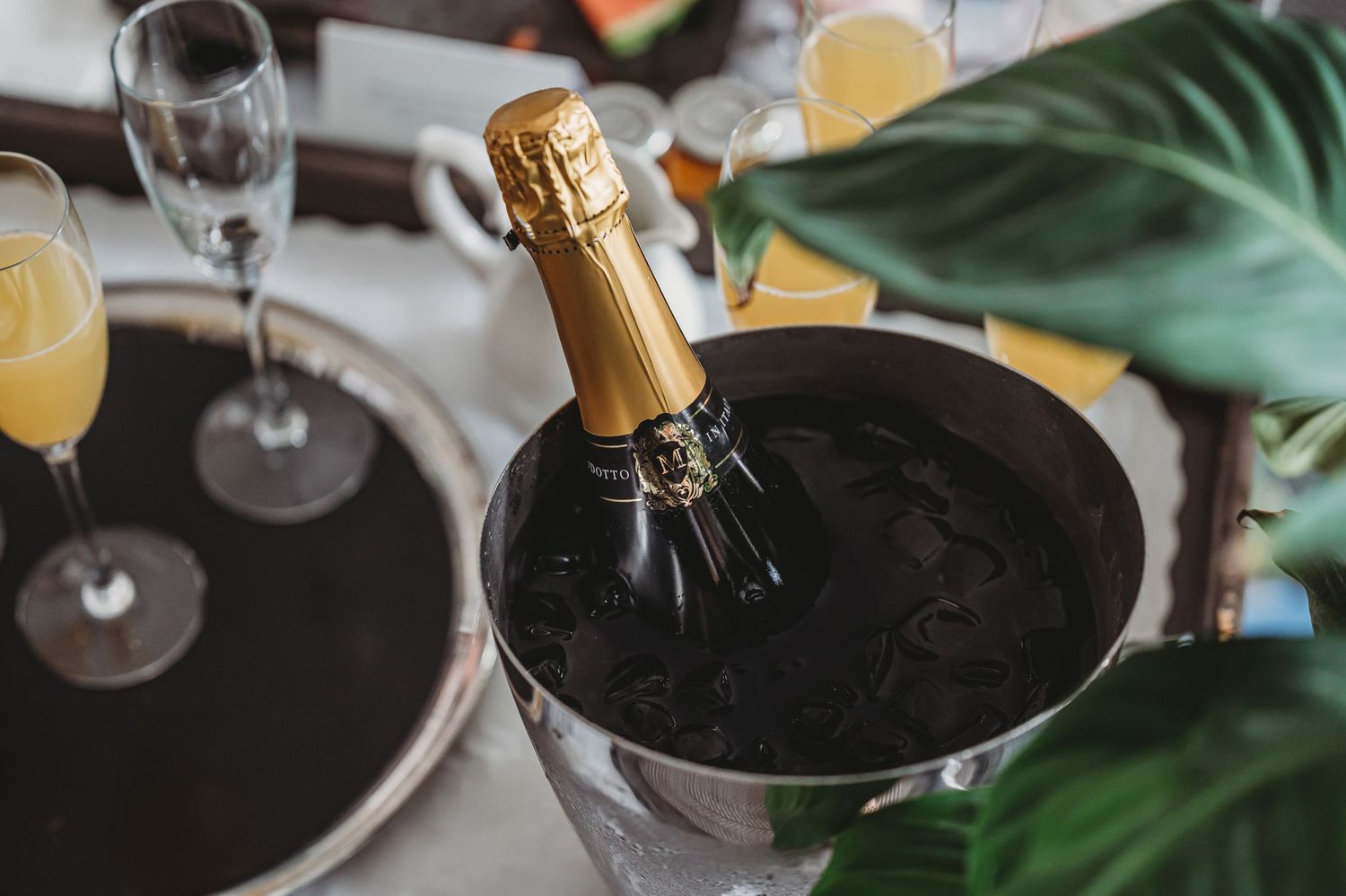 Champagne bottle chilling in an ice bucket with mimosa glasses on a table.