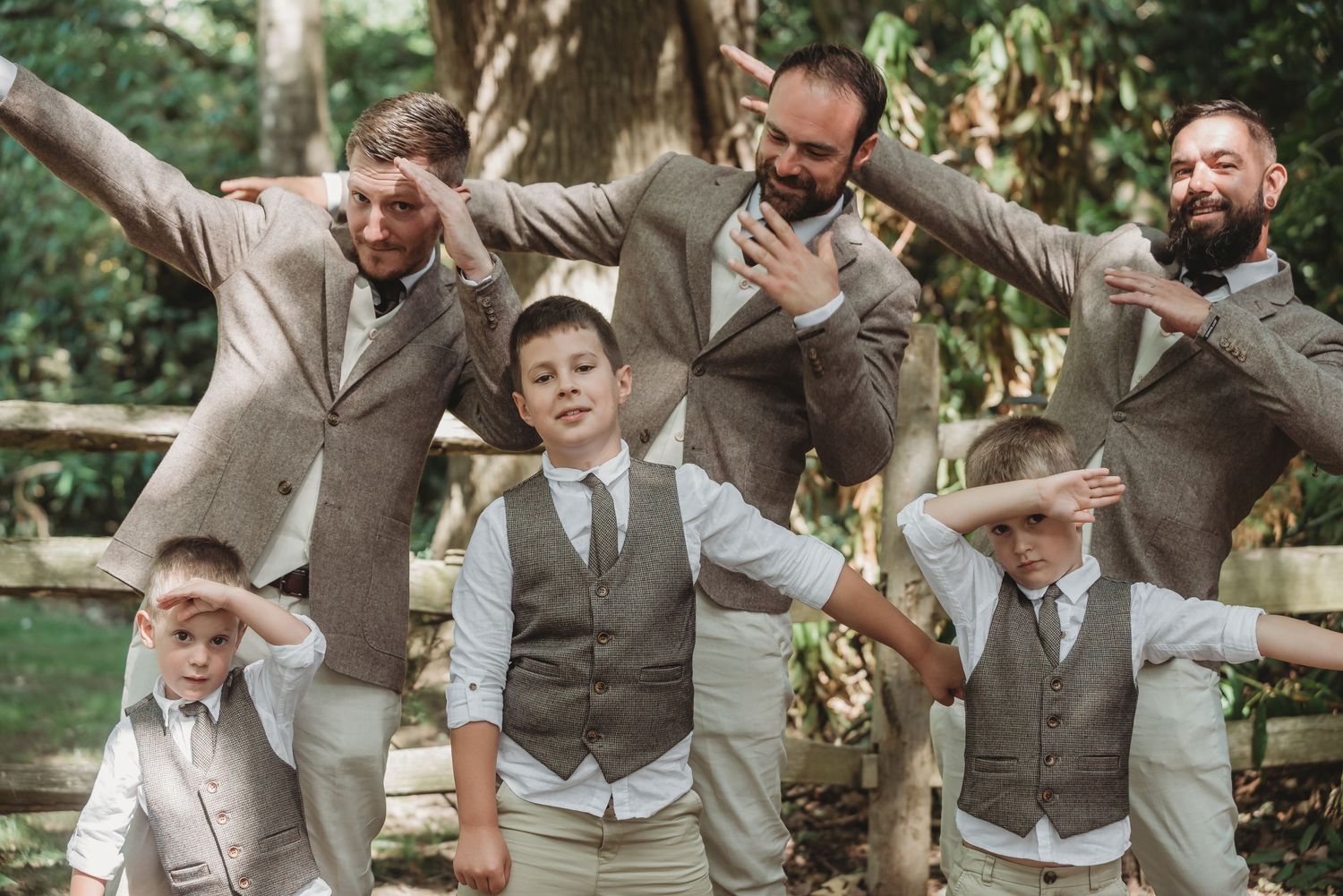Groomsmen in beige suits and vests strike playful poses outdoors.