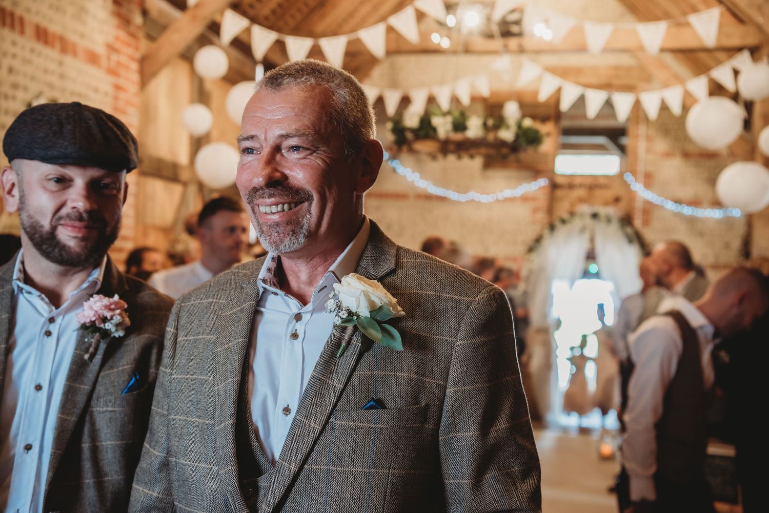 Wedding guest in tweed jacket smiling during indoor reception with bunting decorations.