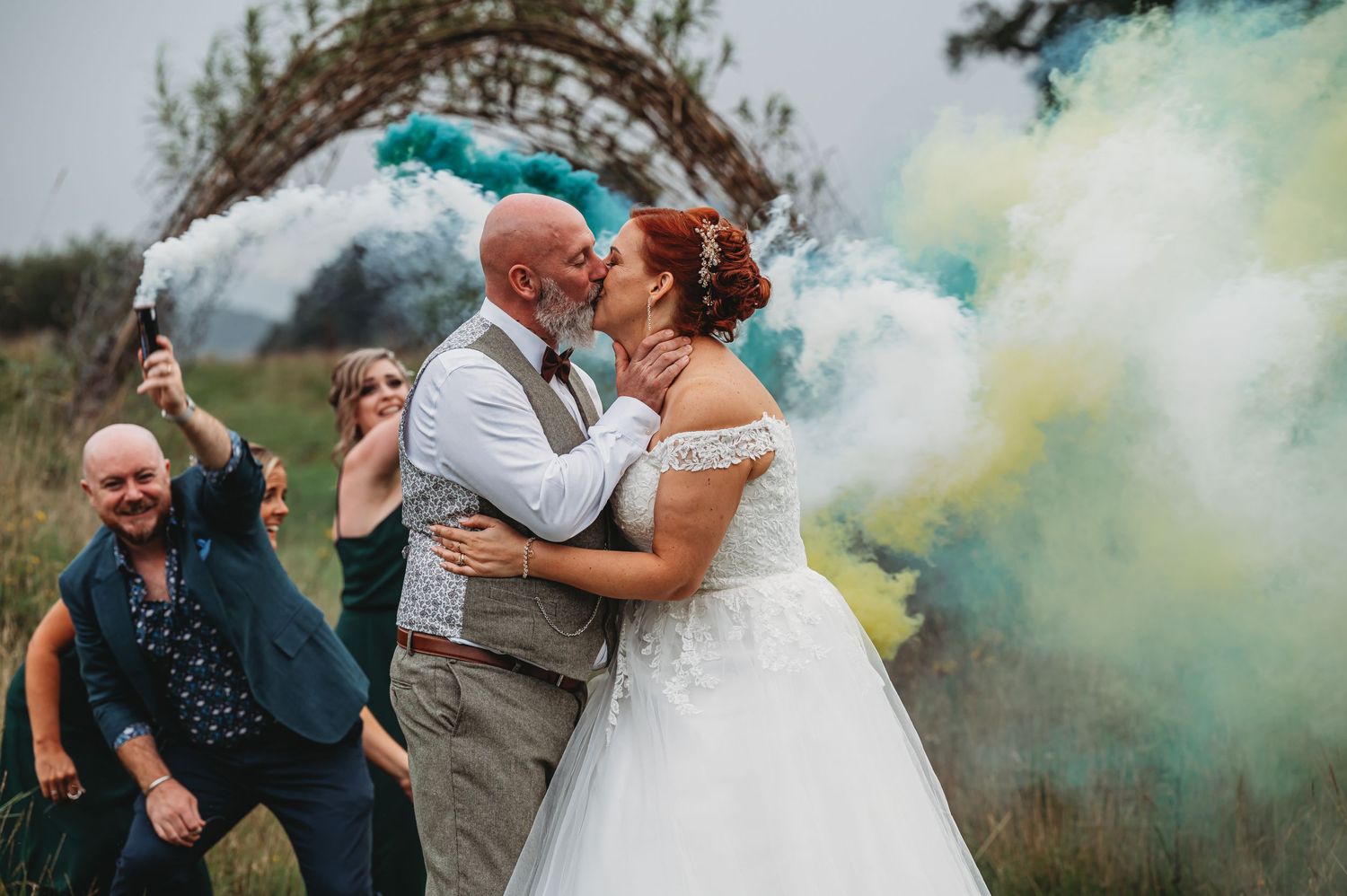 A wedding celebration with colorful smoke bombs creating a vibrant backdrop in an outdoor setting.