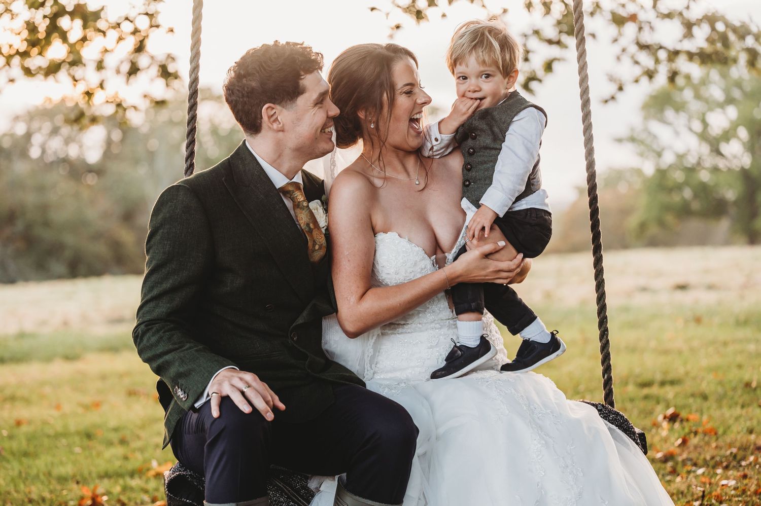 Romantic wedding moment captured on a rustic tree swing in a golden meadow at sunset.