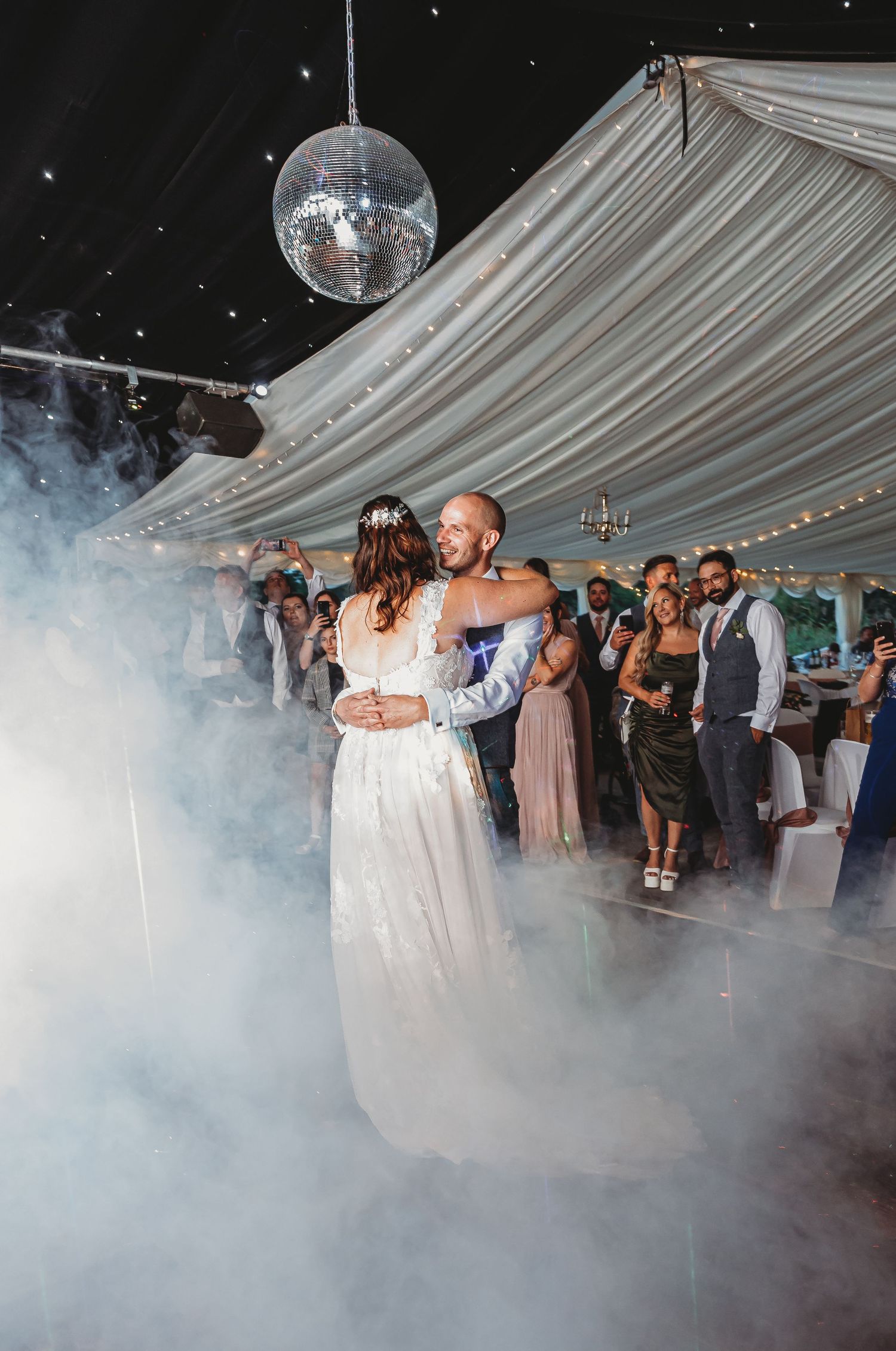 First dance under disco ball with fog machine effects in draped reception tent.