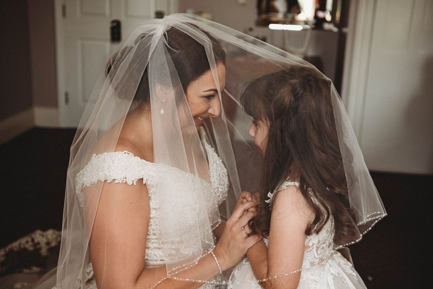 Touching moment shared between two in white dresses under wedding veil.