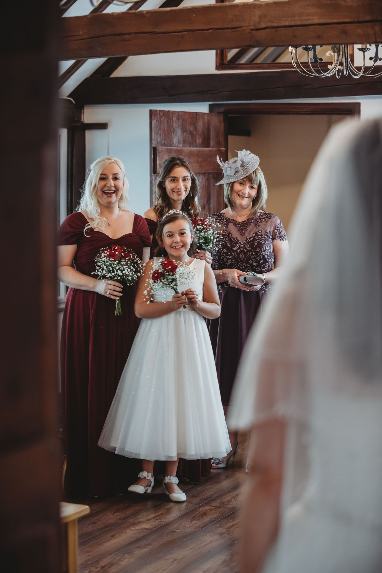 Wedding party members in burgundy dresses and white gown gather together before ceremony in rustic venue.