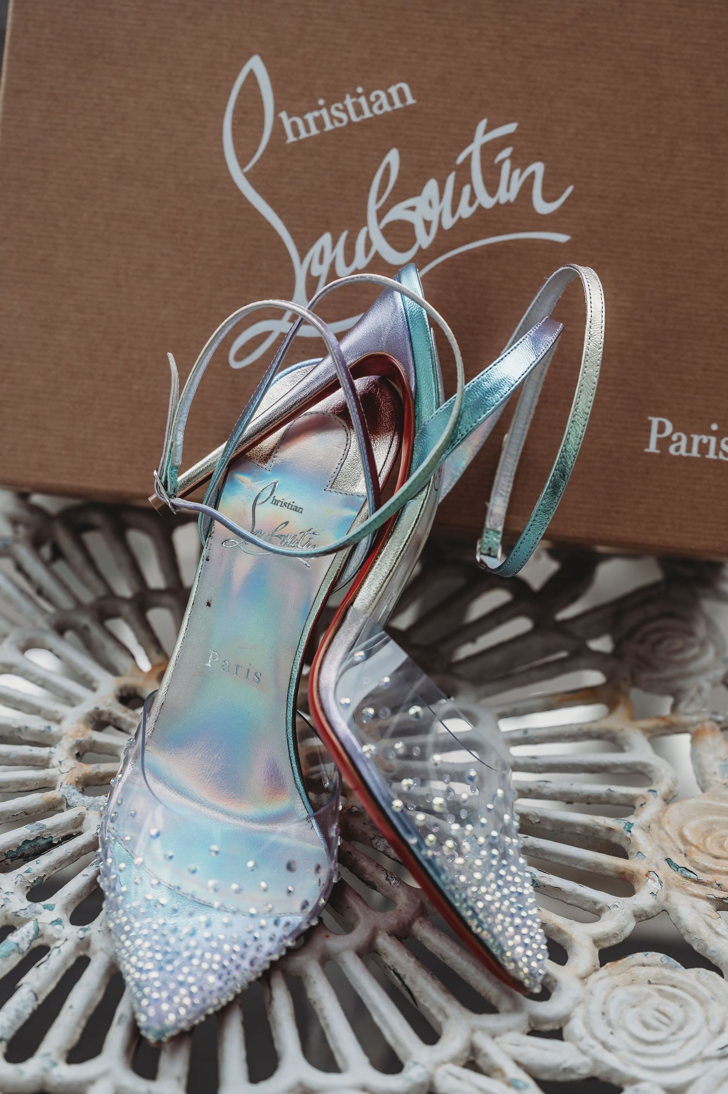 Sparkly Christian Louboutin bridal shoes with crystal details displayed on decorative surface.