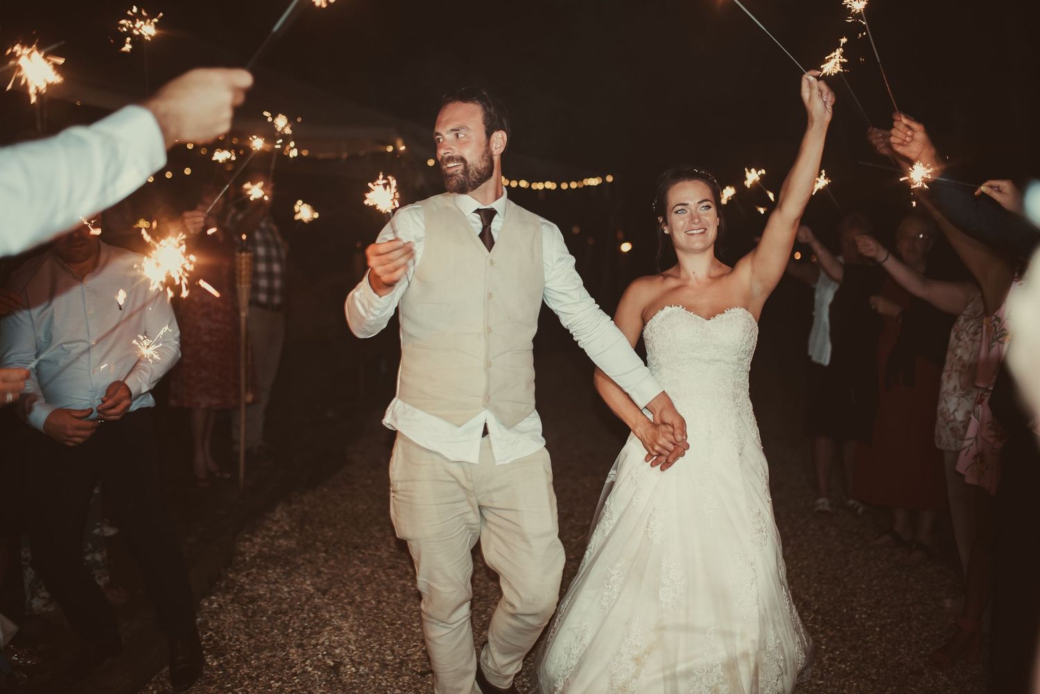 Newlyweds run through a sparkler exit during their nighttime wedding celebration.