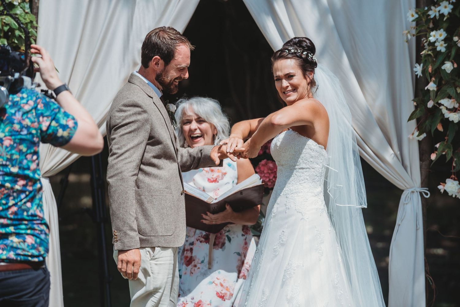 Outdoor wedding ceremony taking place under white fabric arch with laughter and joy.