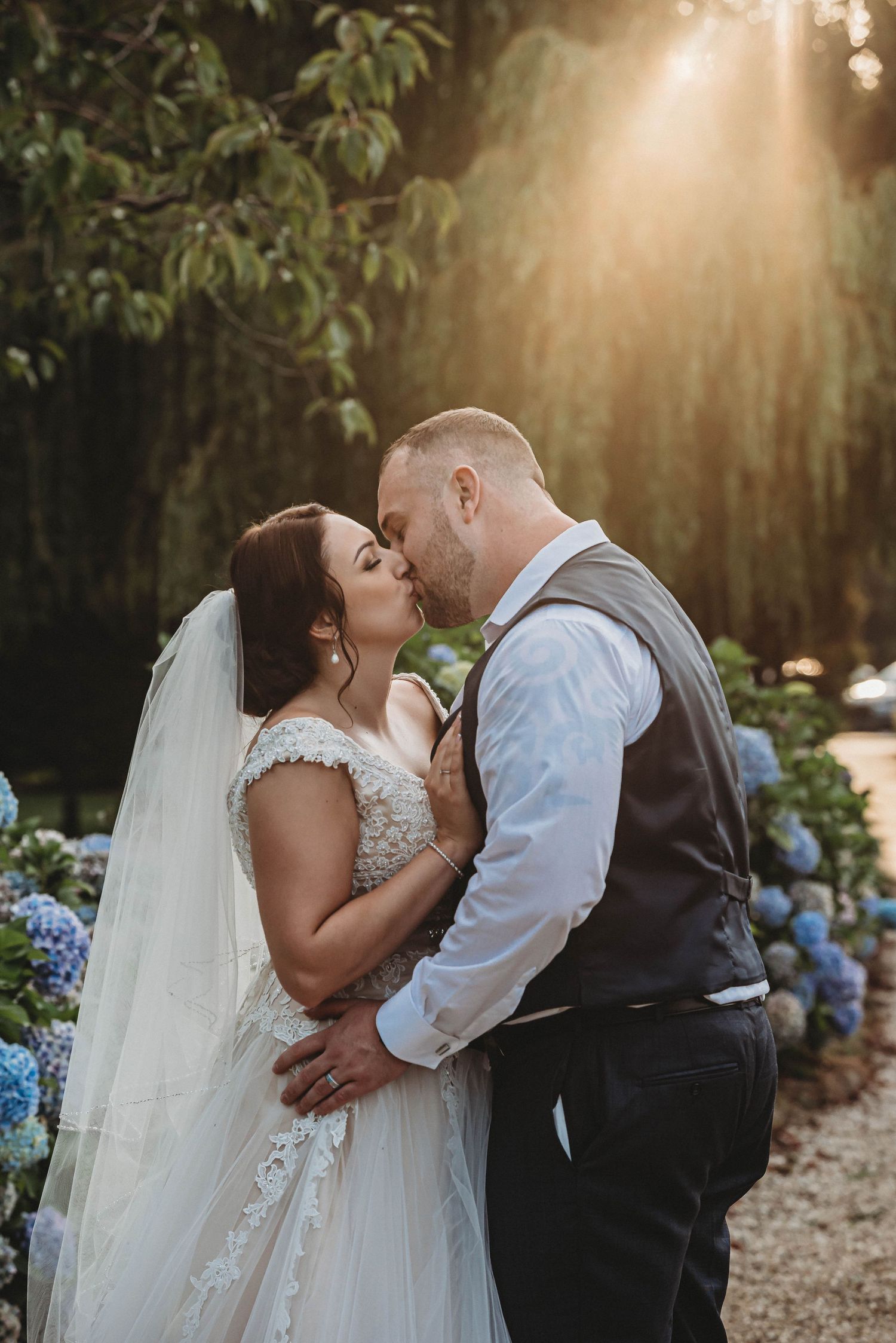A romantic sunset wedding portrait among hydrangeas and dappled evening light.
