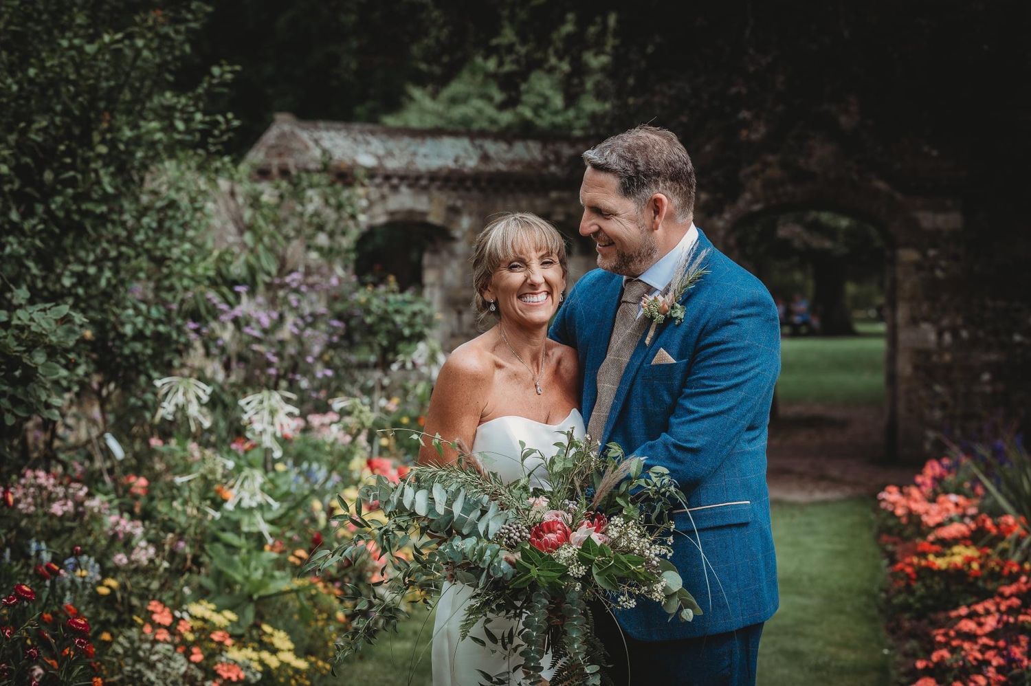 A couple poses in a blooming garden with colorful flowers and greenery.