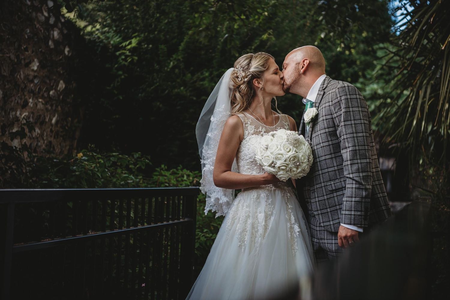 Couple shares intimate moment in garden setting with bride holding white bouquet.