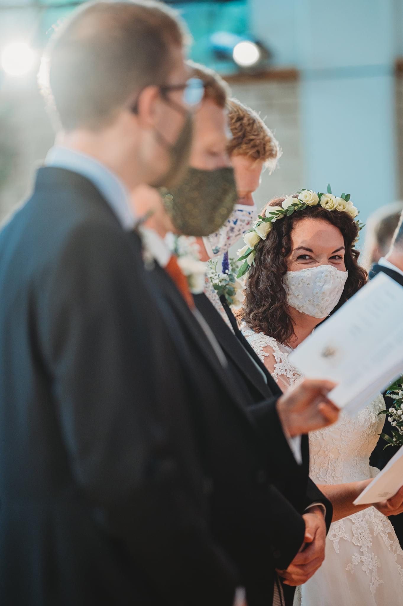 A masked wedding ceremony during Covid-19 with attendees gathered indoors.