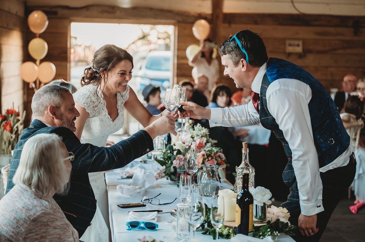 Wedding reception scene with newlyweds toasting guests at a rustic wooden venue.