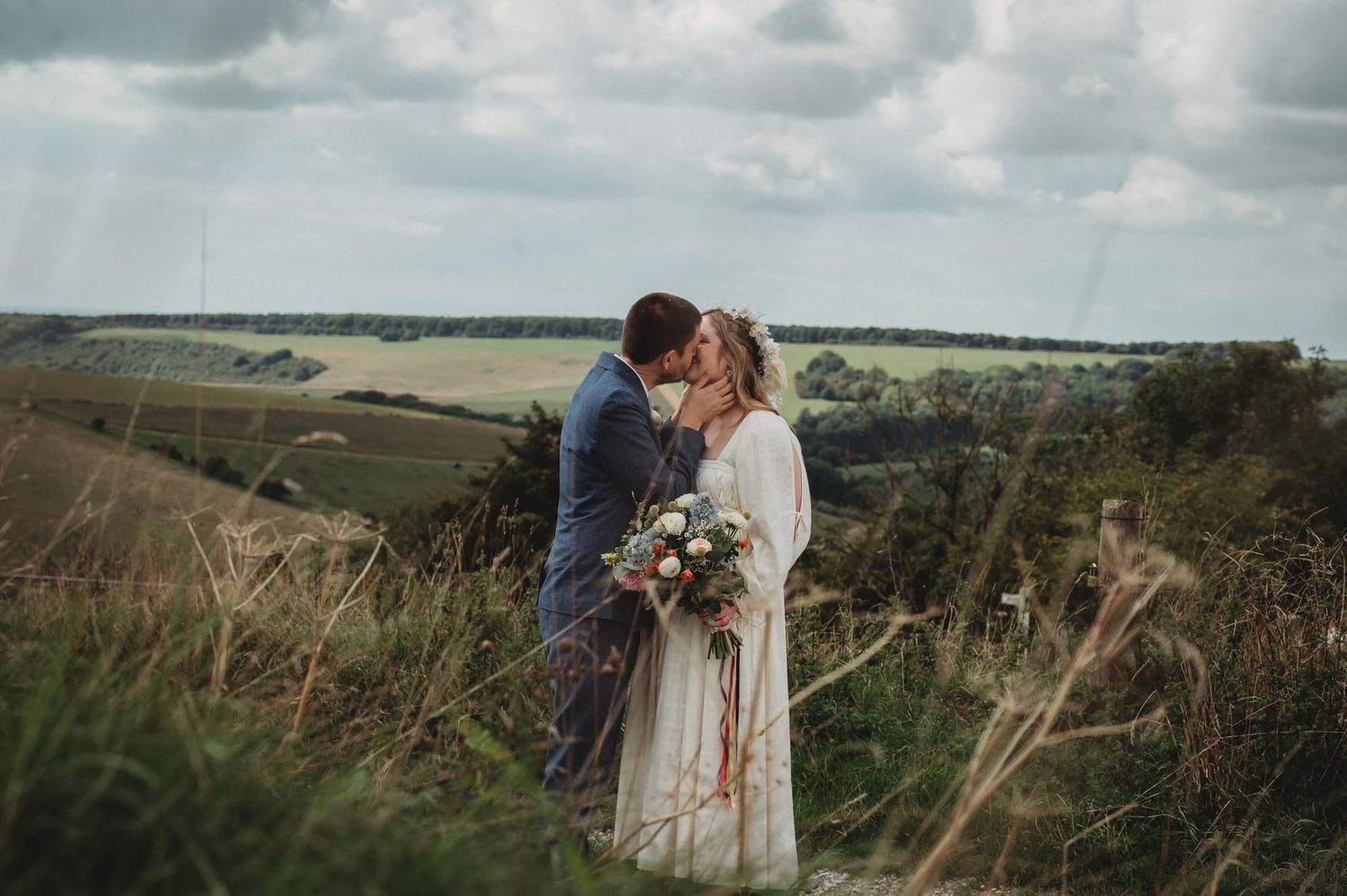 A couple shares a romantic moment on a hilltop overlooking rolling countryside.