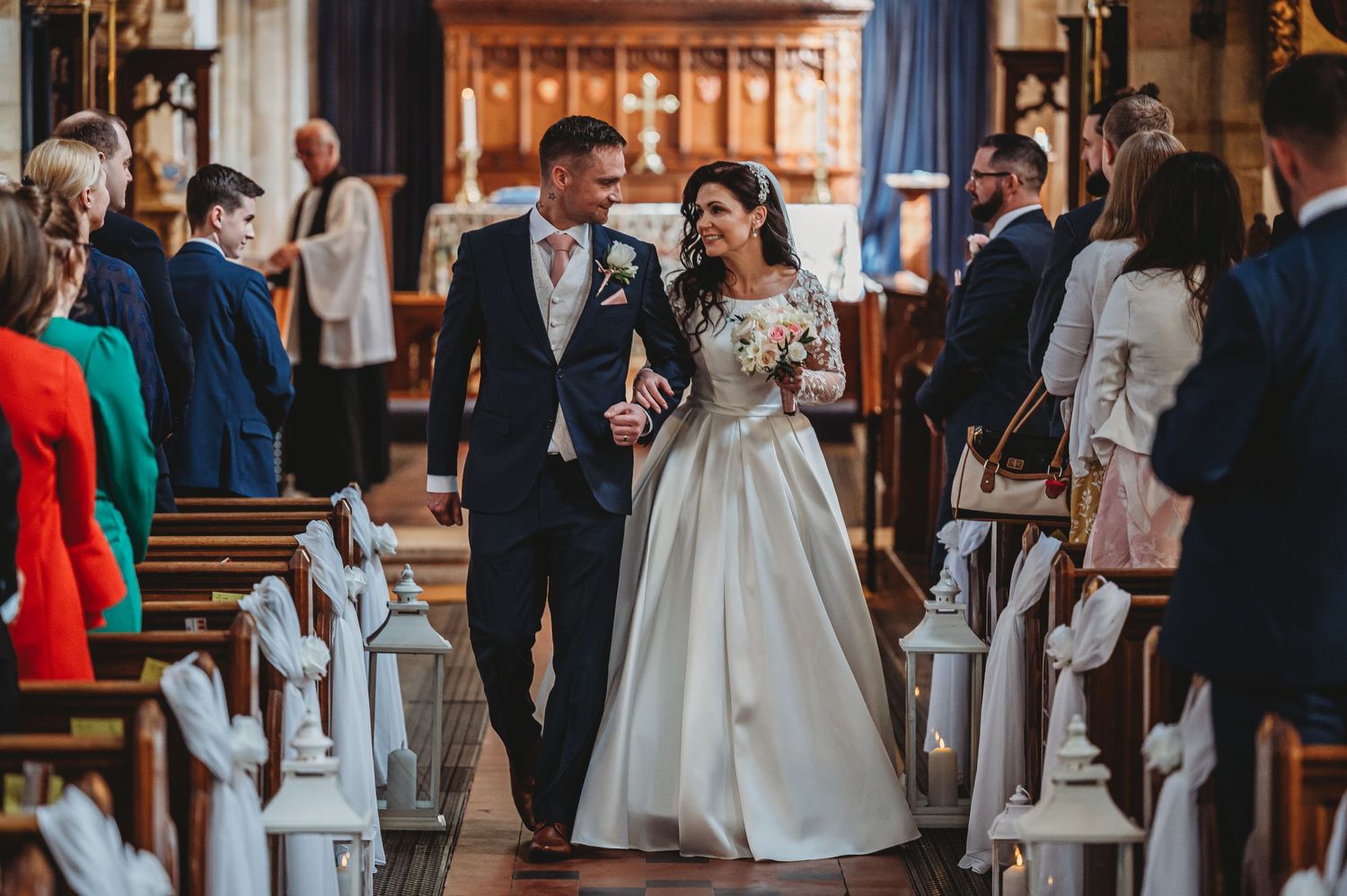 Wedding couple walking down church aisle after ceremony while guests look on.