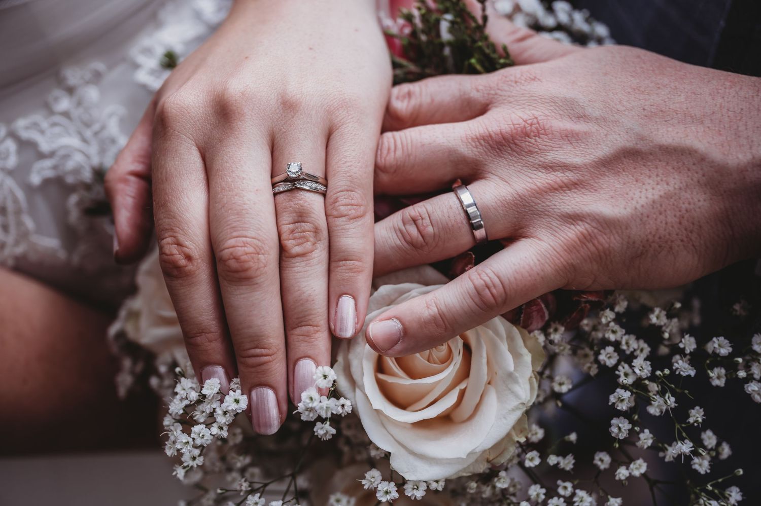 Close-up of wedding rings on hands with a rose and baby's breath flowers.