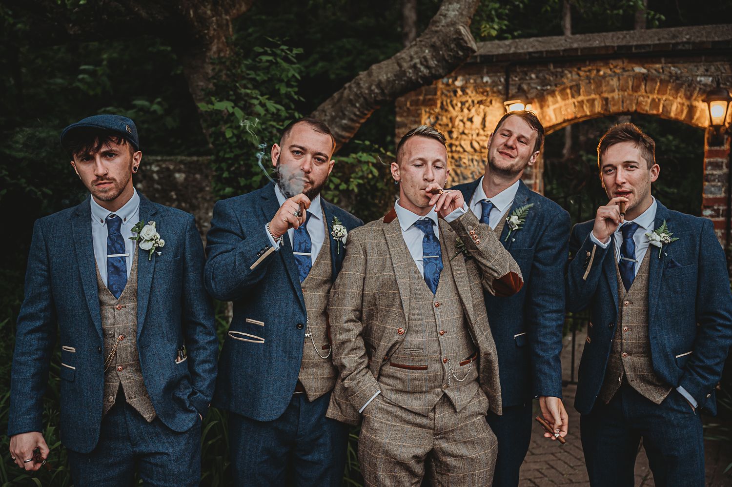 Groomsmen in navy suits and tan vests pose playfully for a wedding photo.