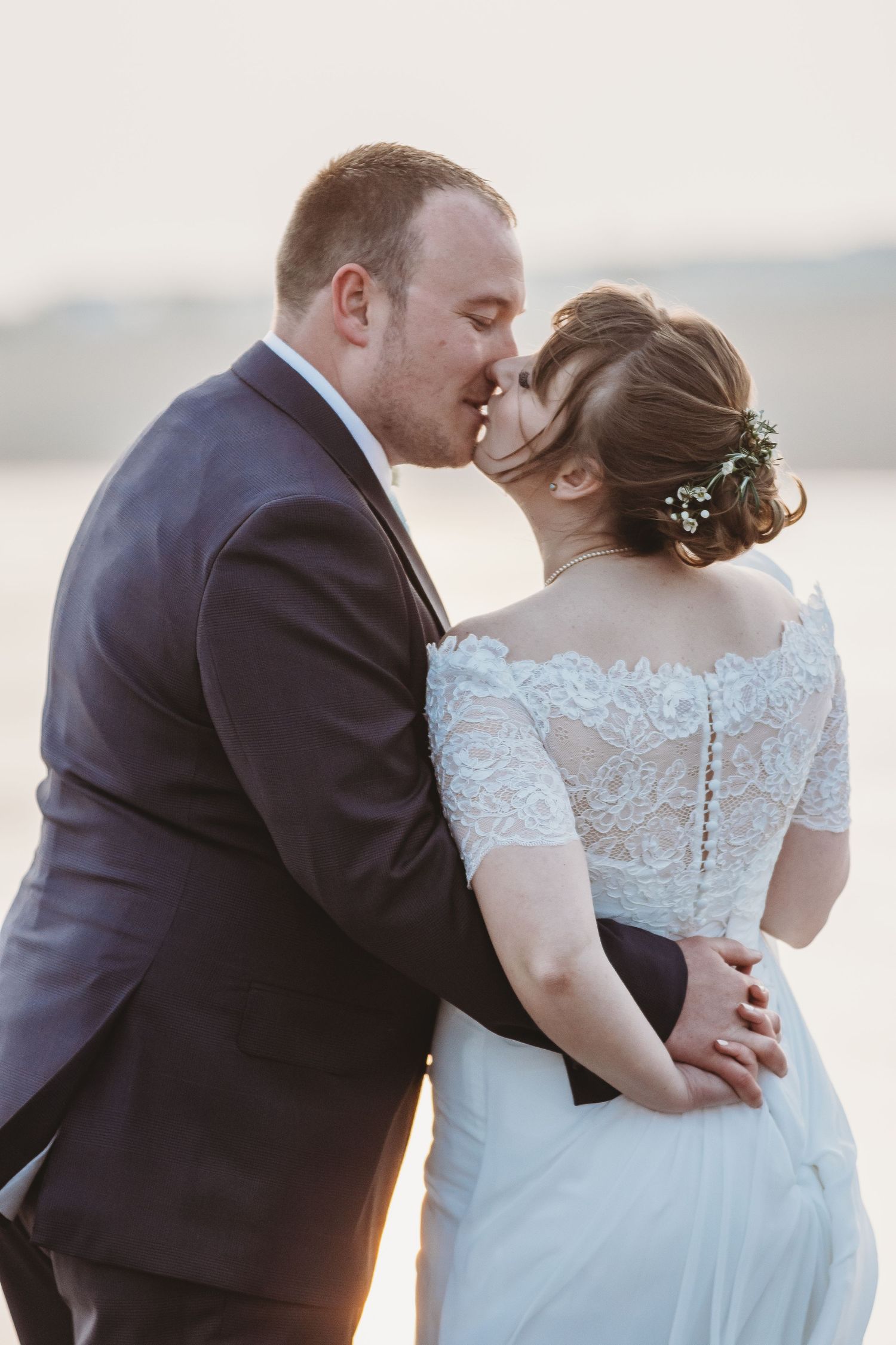Intimate moment between newlyweds, with focus on the bride's detailed lace back dress.