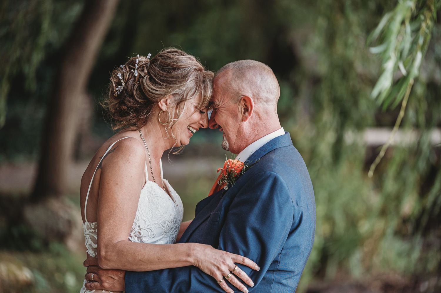 Tender moment between newlyweds in garden setting with willow trees.