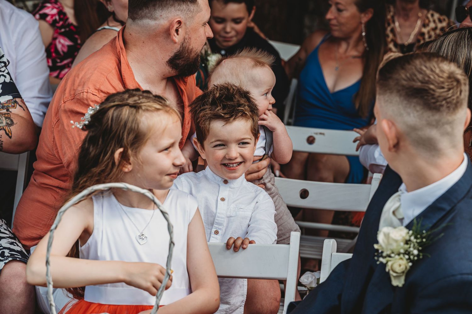 Children laughing together at outdoor wedding ceremony with guests in background.