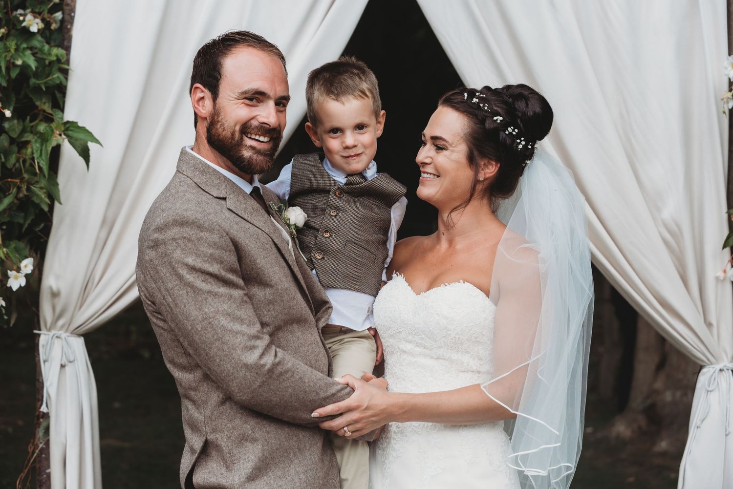 Wedding ceremony moment under white draped arch with greenery.