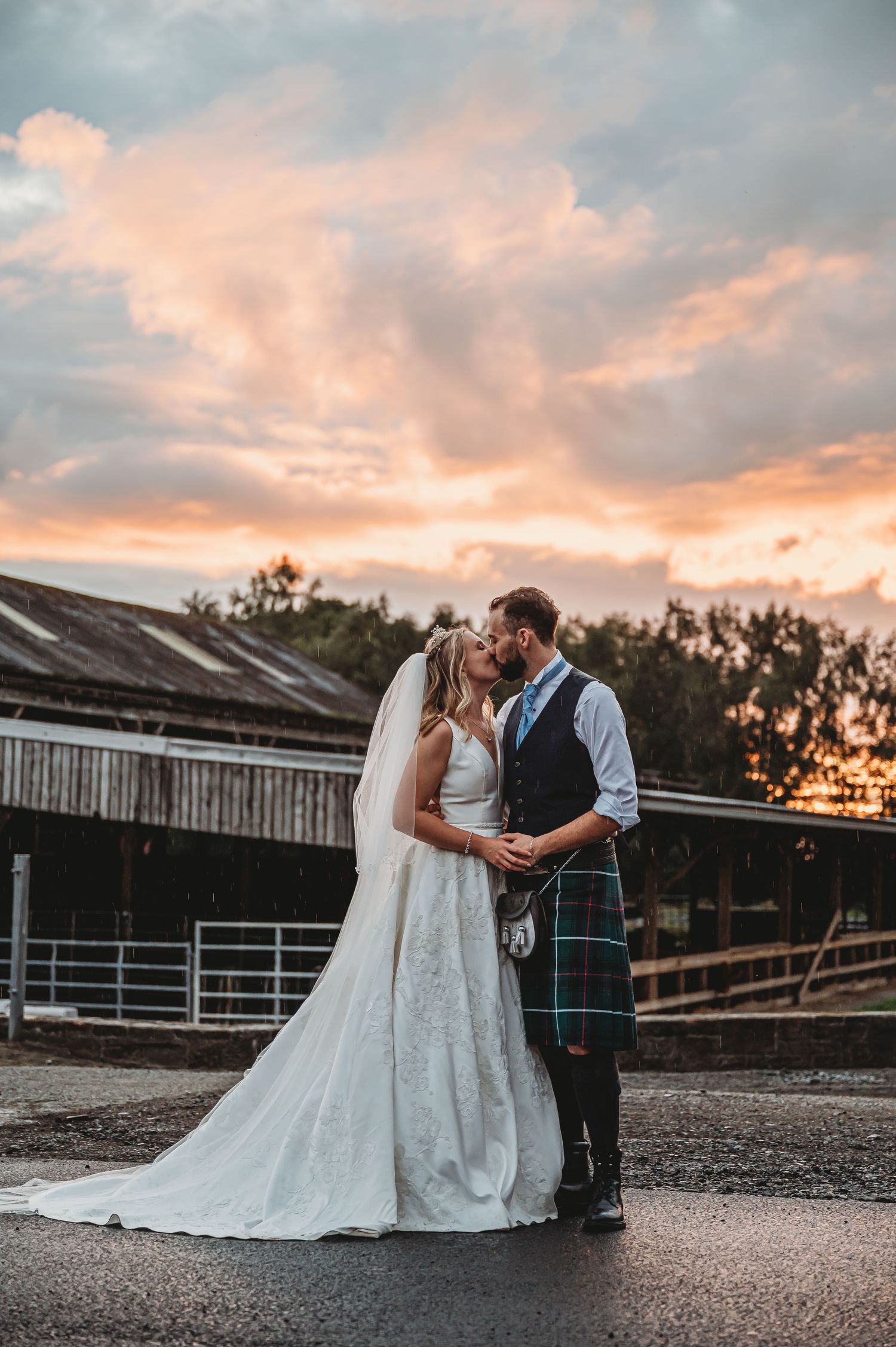 Romantic sunset wedding photo at rustic barn venue with dramatic sky.