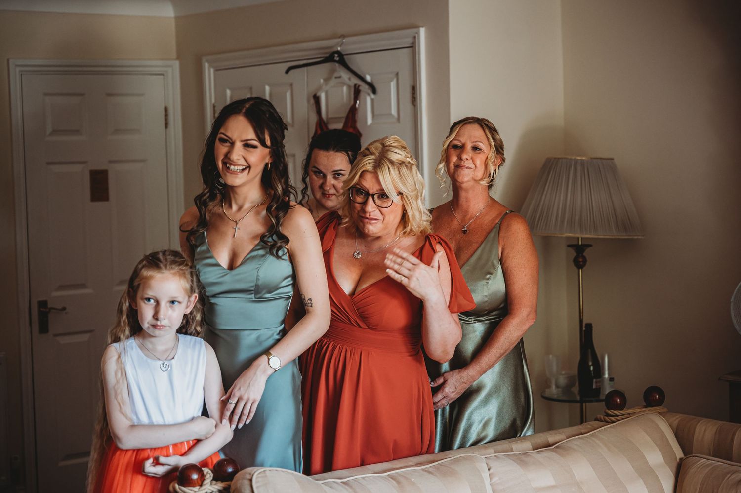 Candid getting-ready moment with wedding party in pastel dresses in a brightly lit room.