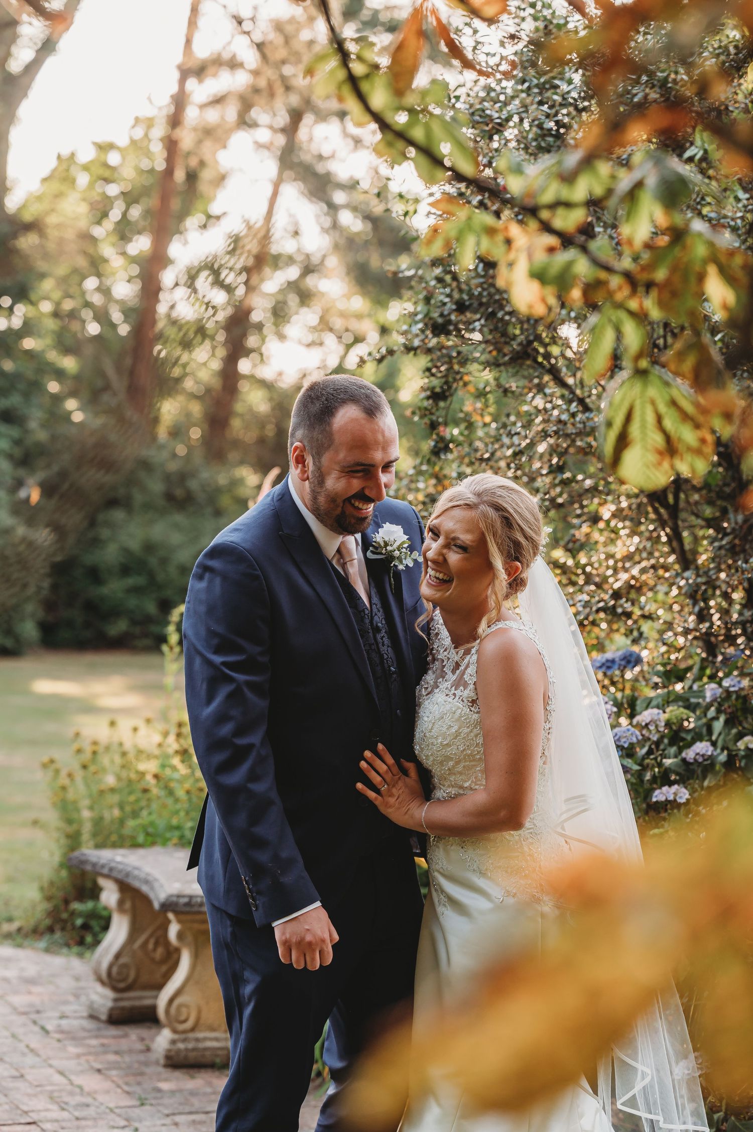 Couple shares a joyful moment in a garden setting with sunlight filtering through the trees.