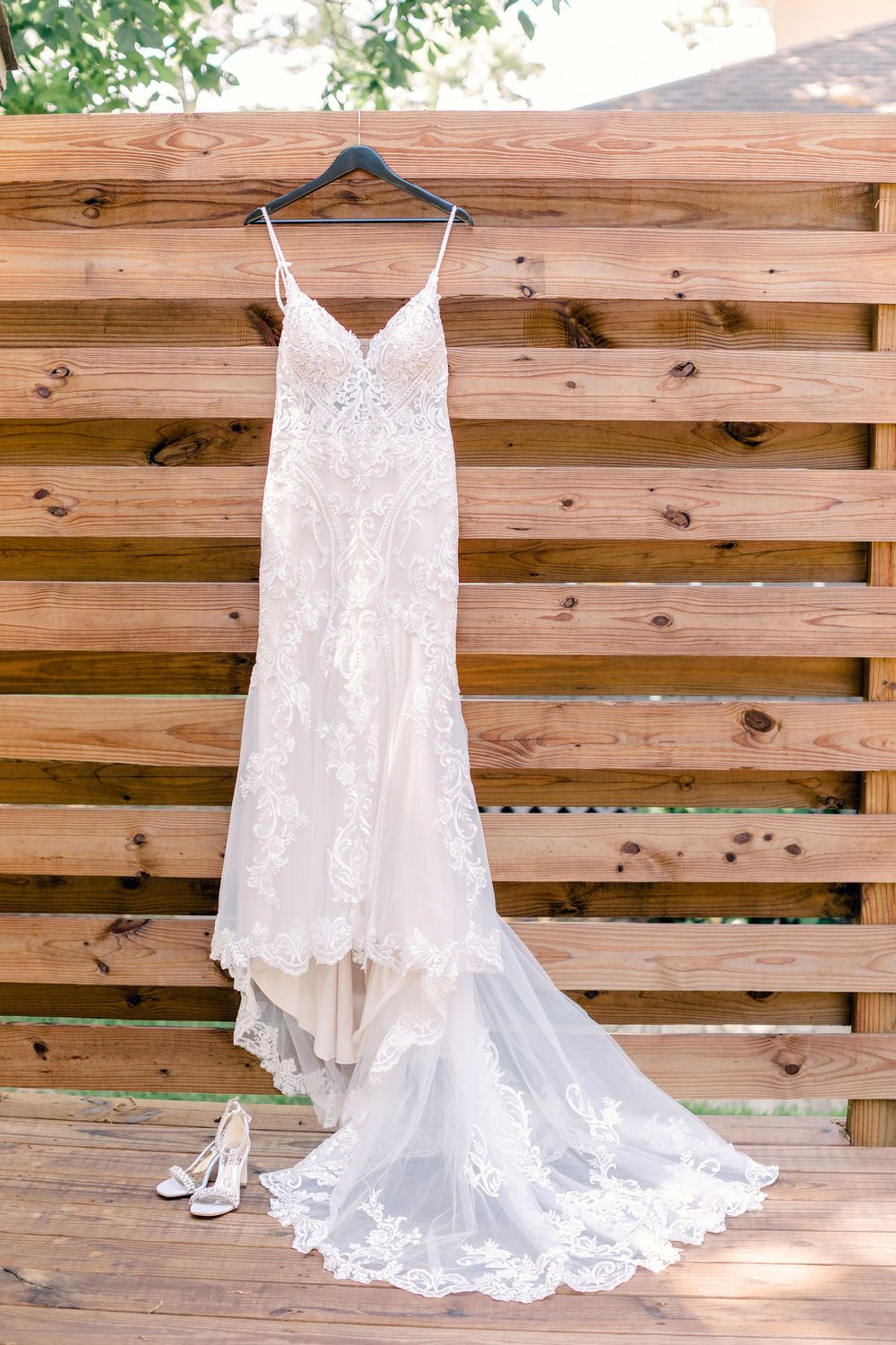 Elegant lace wedding dress with long train hanging on wooden wall display.