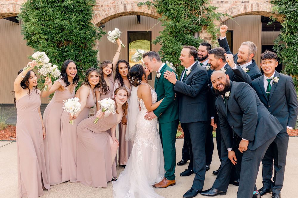 Wedding party photo with bridesmaids in pink dresses and groomsmen in dark suits celebrating.