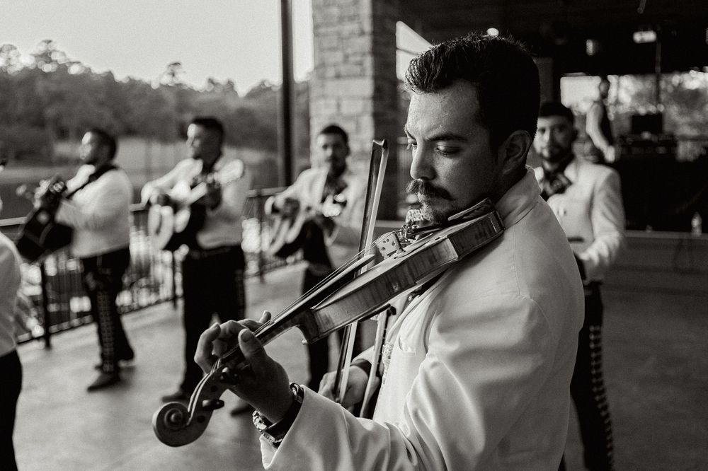 A musician in white plays violin with band members performing in the background.