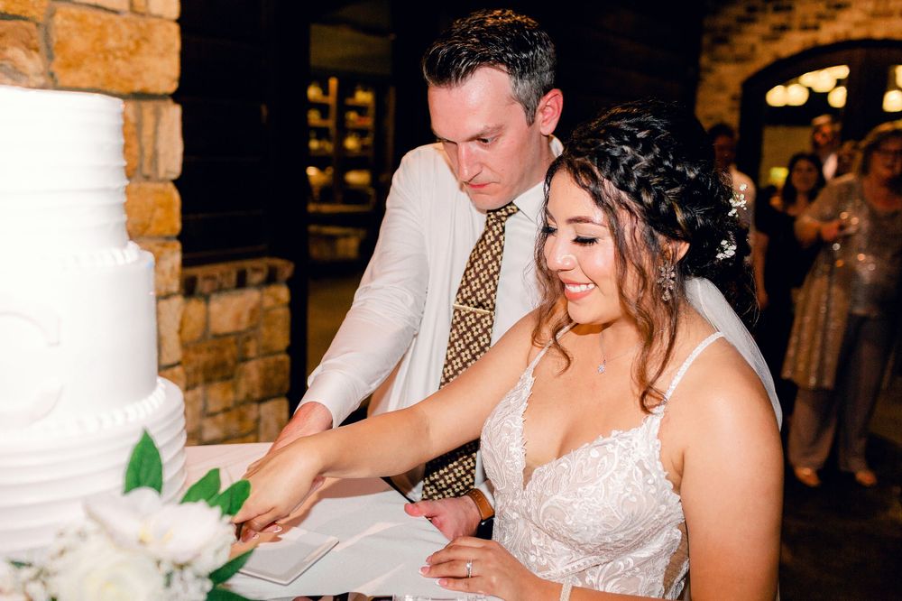 A couple cuts their white wedding cake together in a rustic brick venue setting.