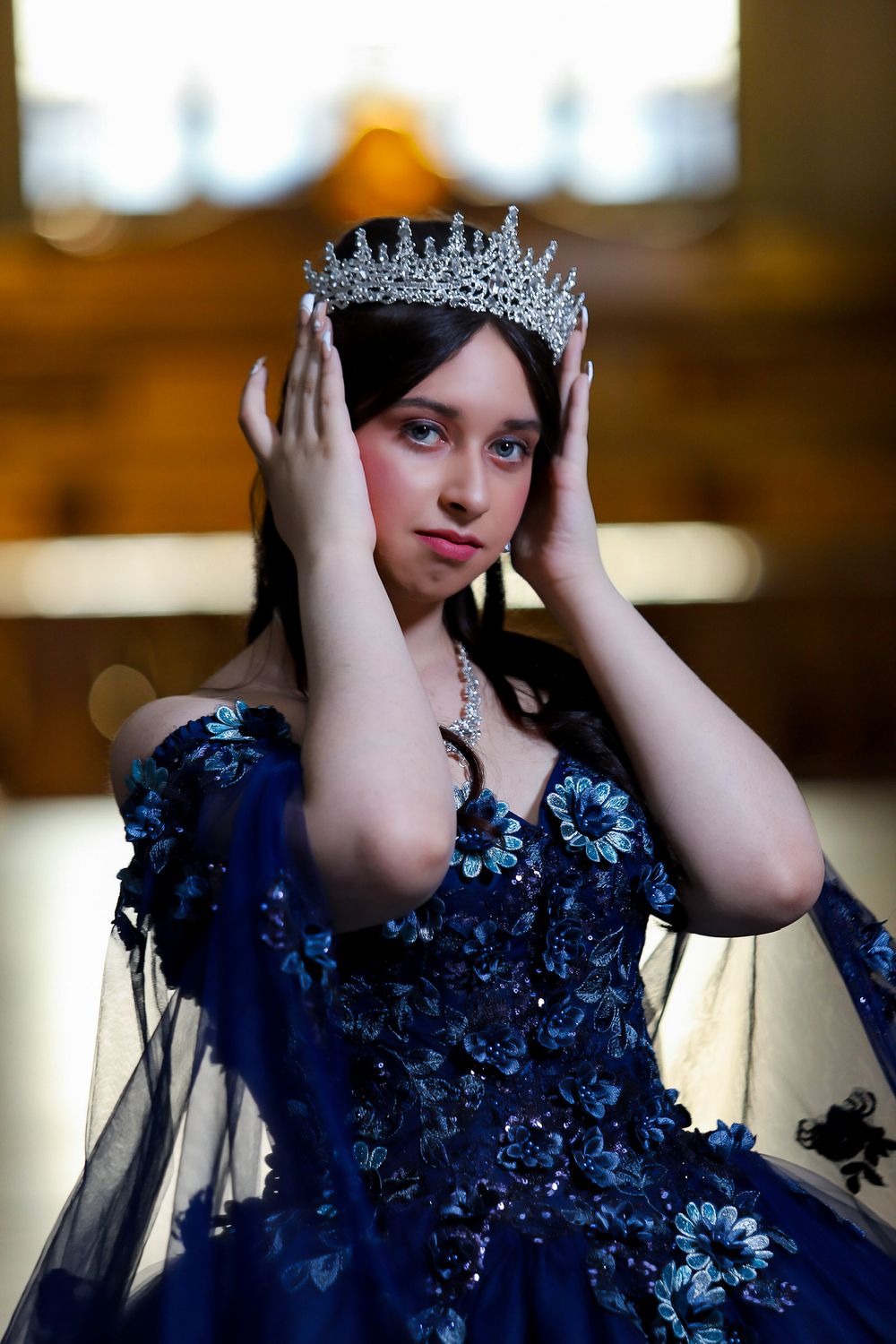 A sparkling crystal crown adorns a formal navy blue gown for a celebration portrait.
