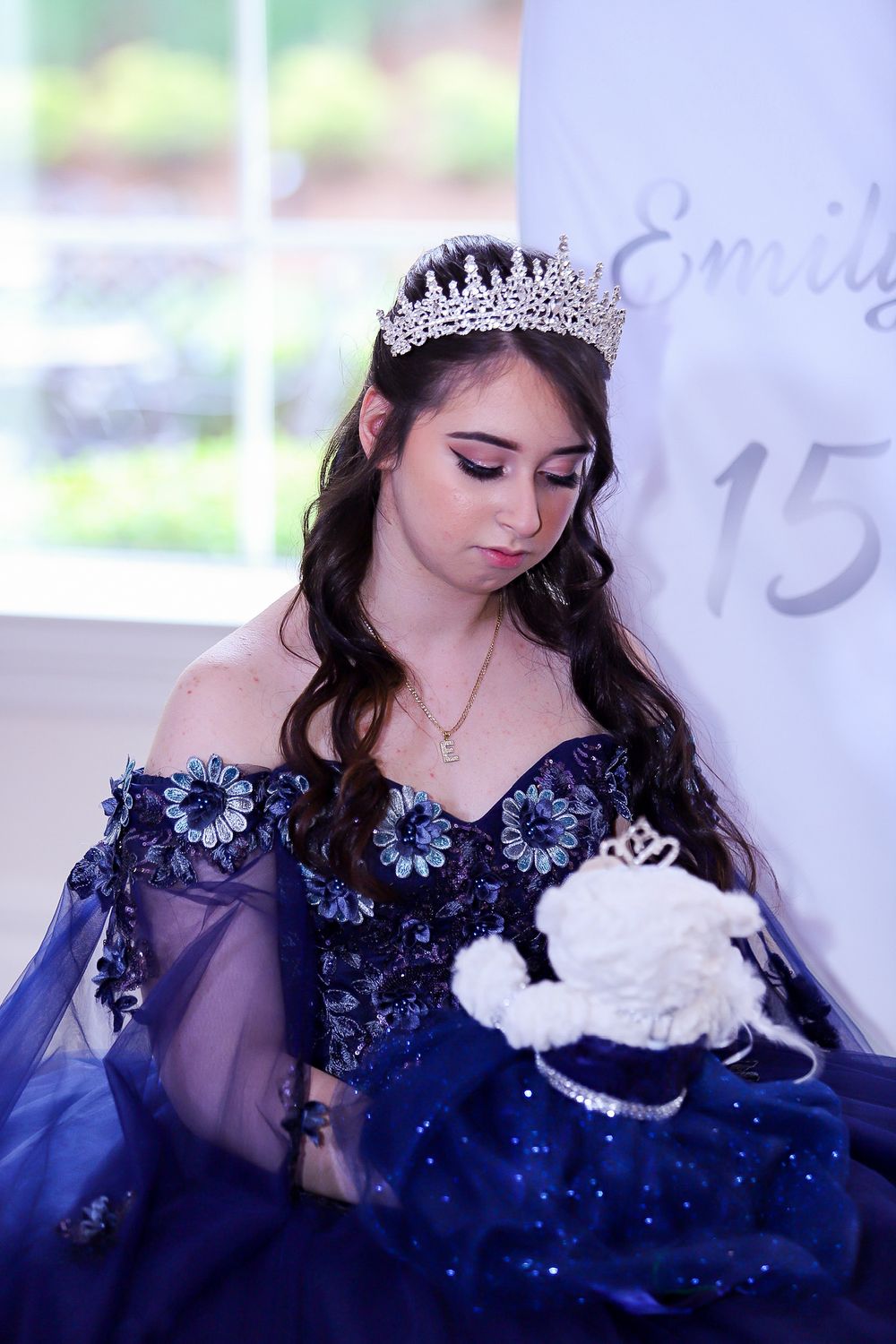 An elegant navy blue ball gown with off-shoulder design and crystal tiara create a regal celebration look.