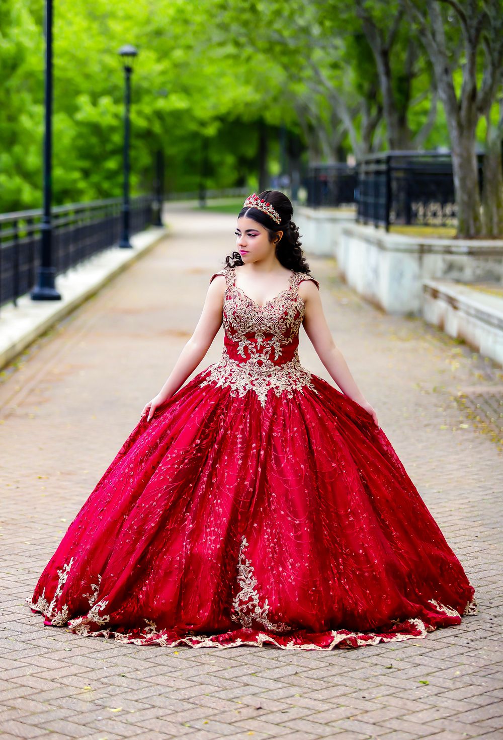 A stunning red and gold ball gown with intricate embroidery photographed on a tree-lined pathway.