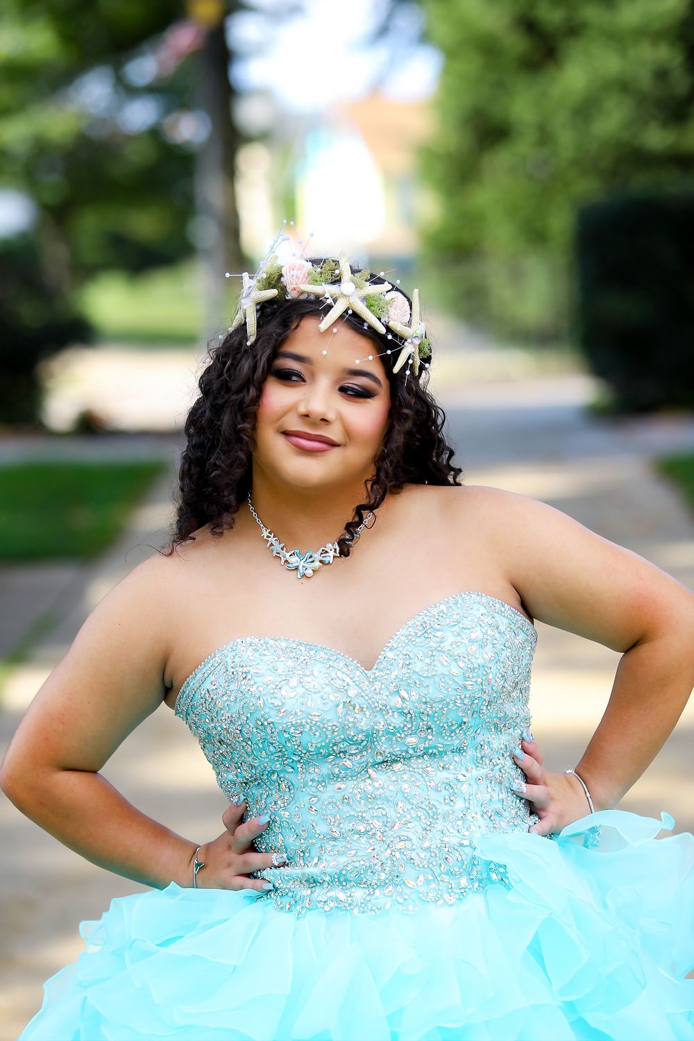 A celebrant poses outdoors in a beaded turquoise gown and delicate floral crown.