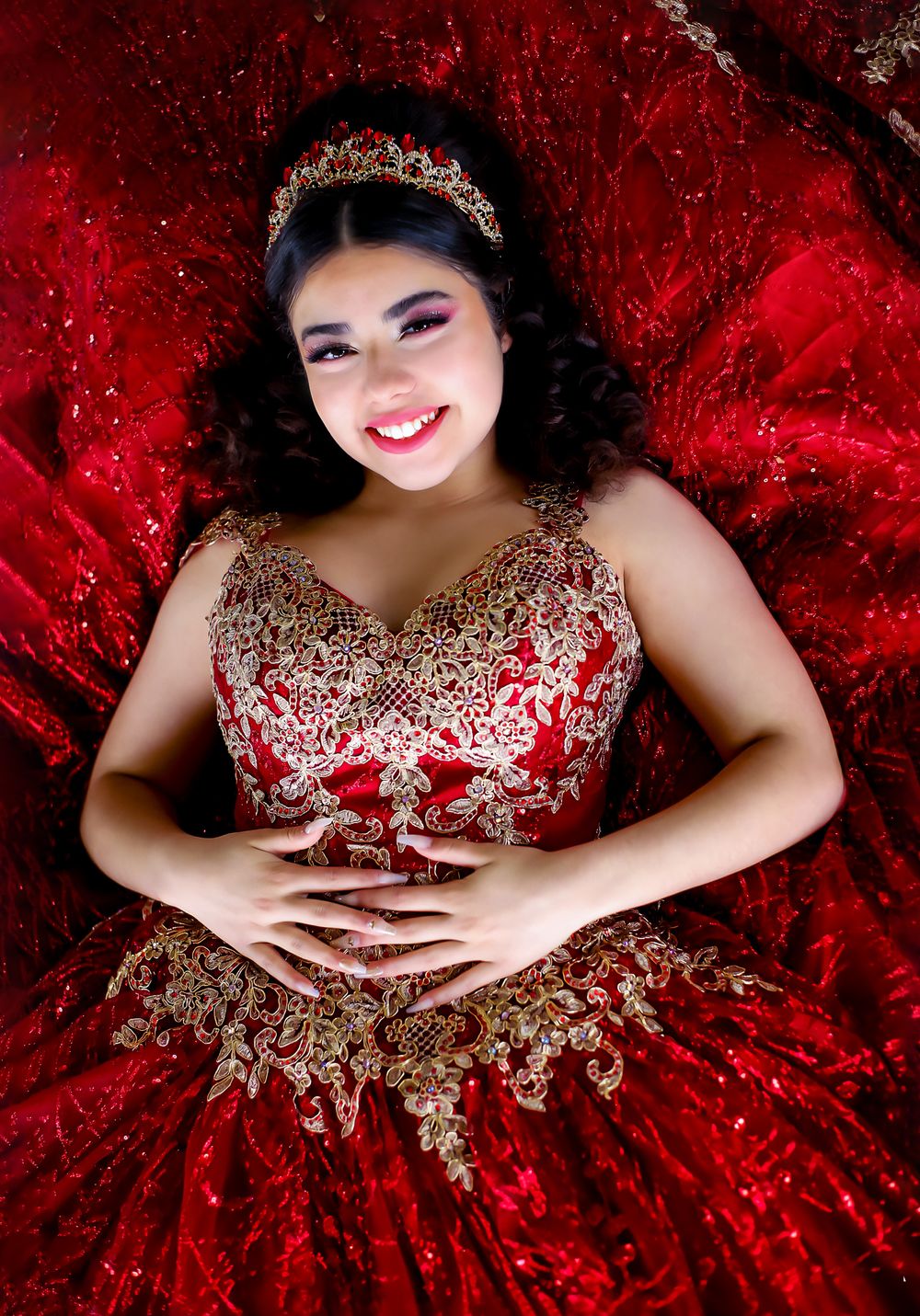 An elegant portrait featuring a red and gold ball gown with detailed beadwork against a crimson backdrop.
