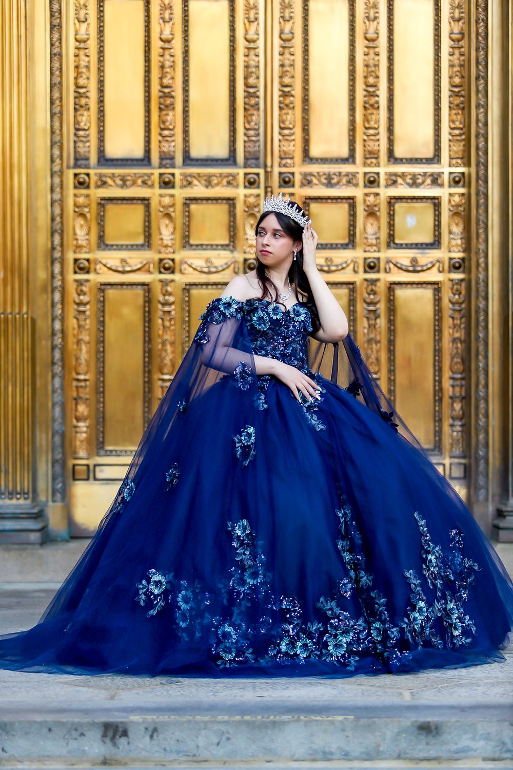 A stunning navy ball gown with floral embellishments photographed against ornate golden doors.