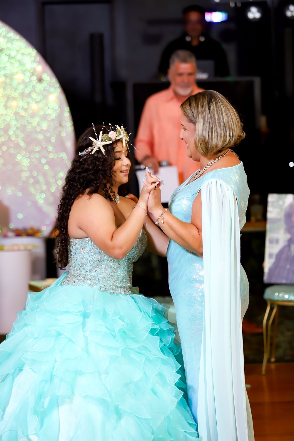 Two people share an emotional moment in matching turquoise formal attire at a celebration.
