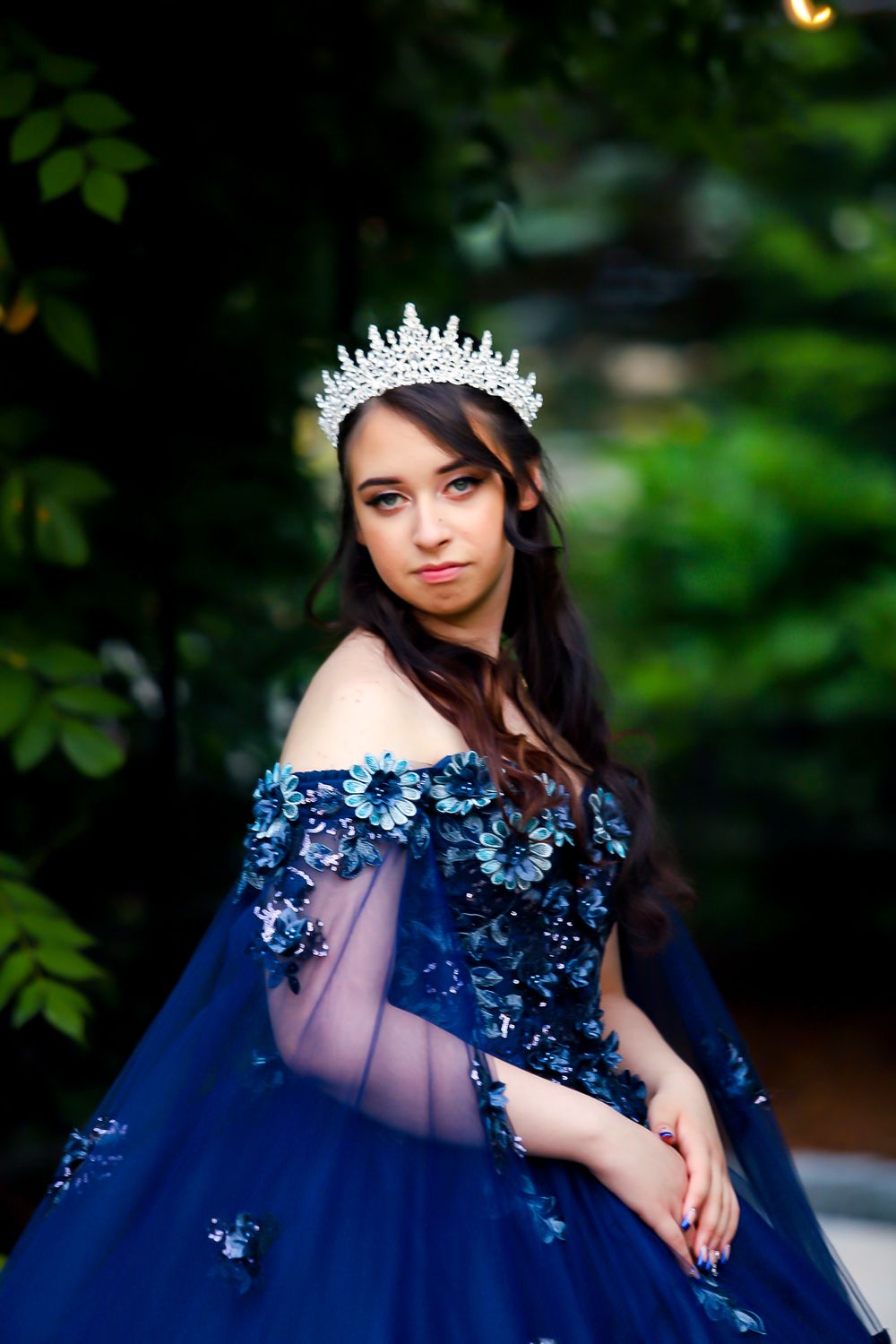 A navy blue ball gown with floral details stands out against lush green foliage.