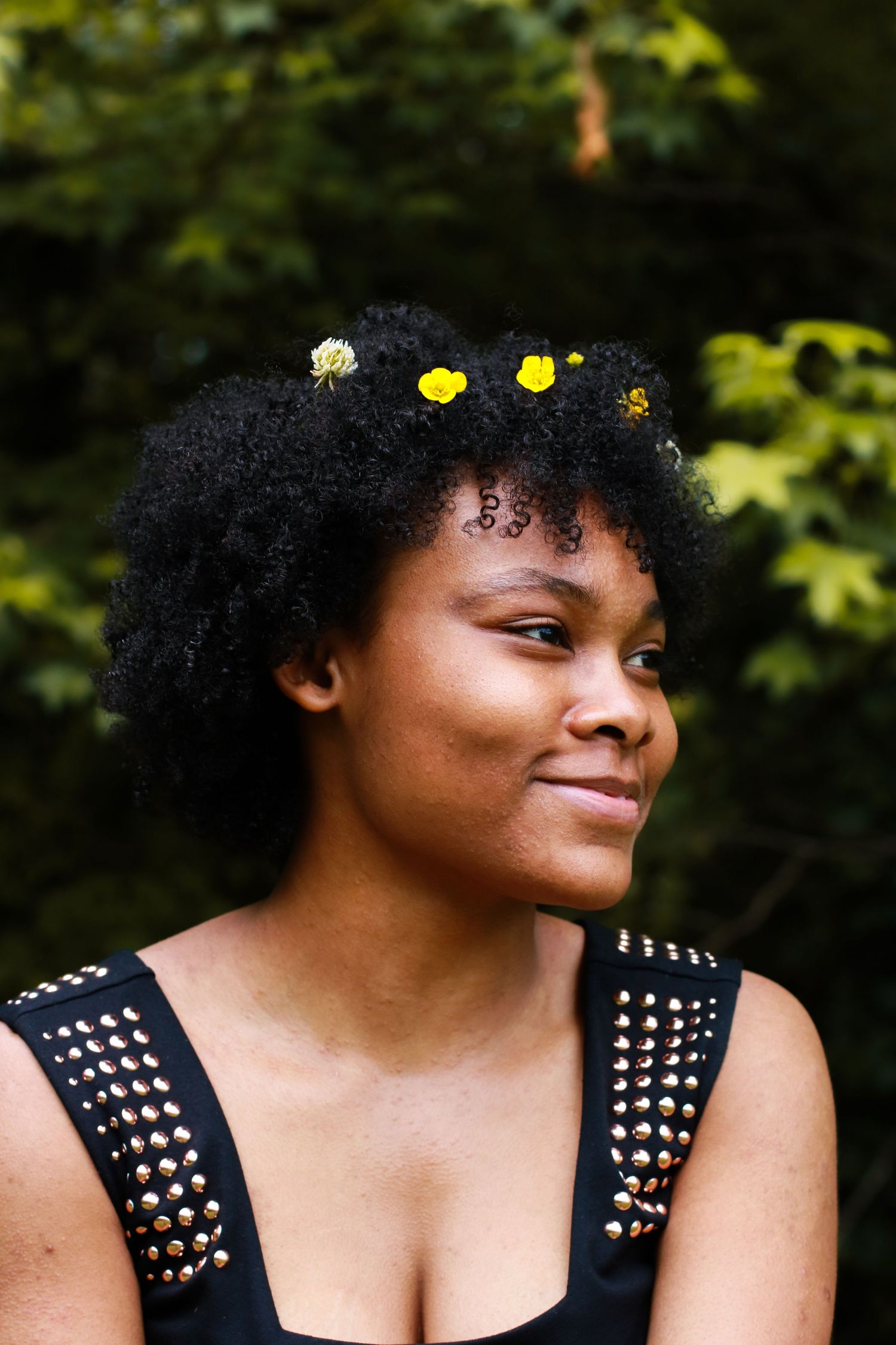 Person with natural curly hair adorned with yellow flowers smiles in outdoor portrait.