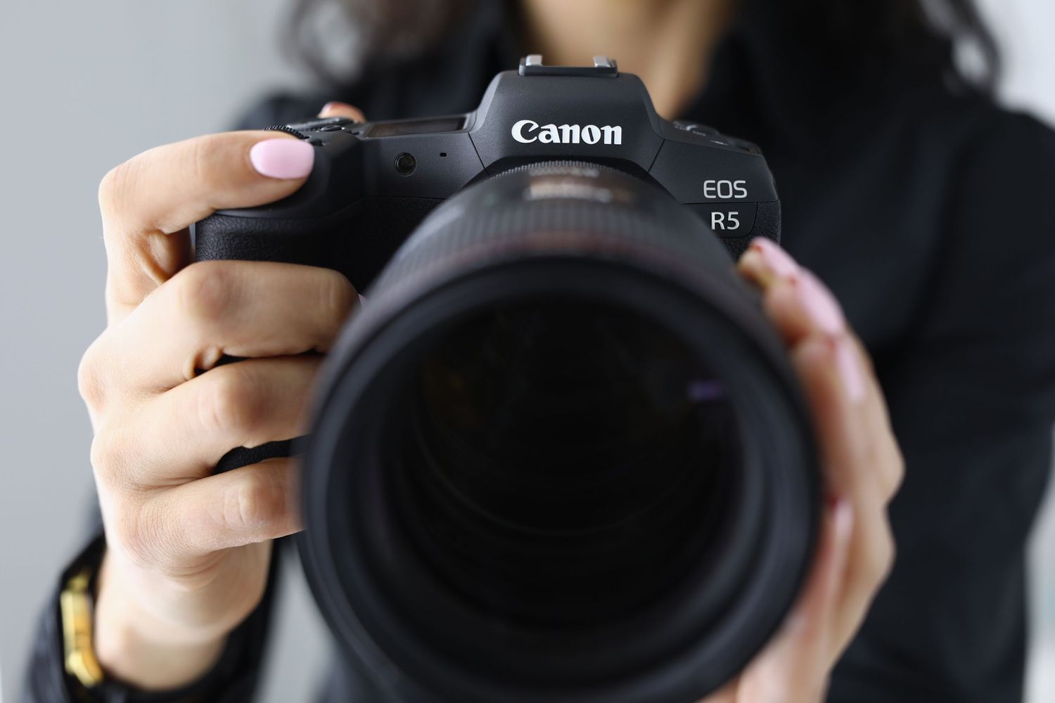 Close-up shot of hands holding a Canon EOS R5 camera with large lens.