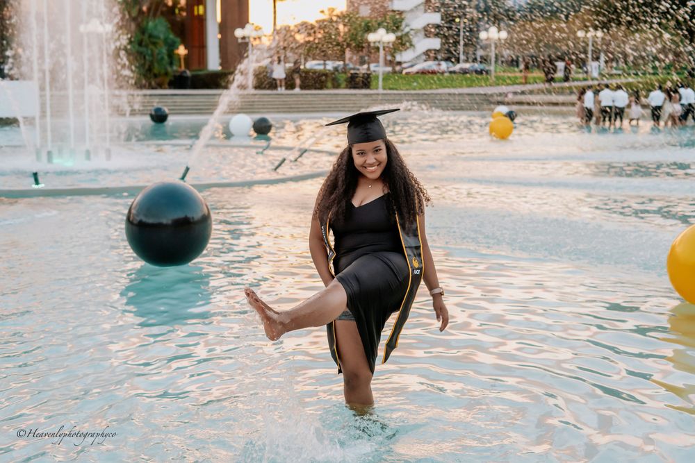 Graduate playfully posing in a campus fountain wearing graduation regalia.