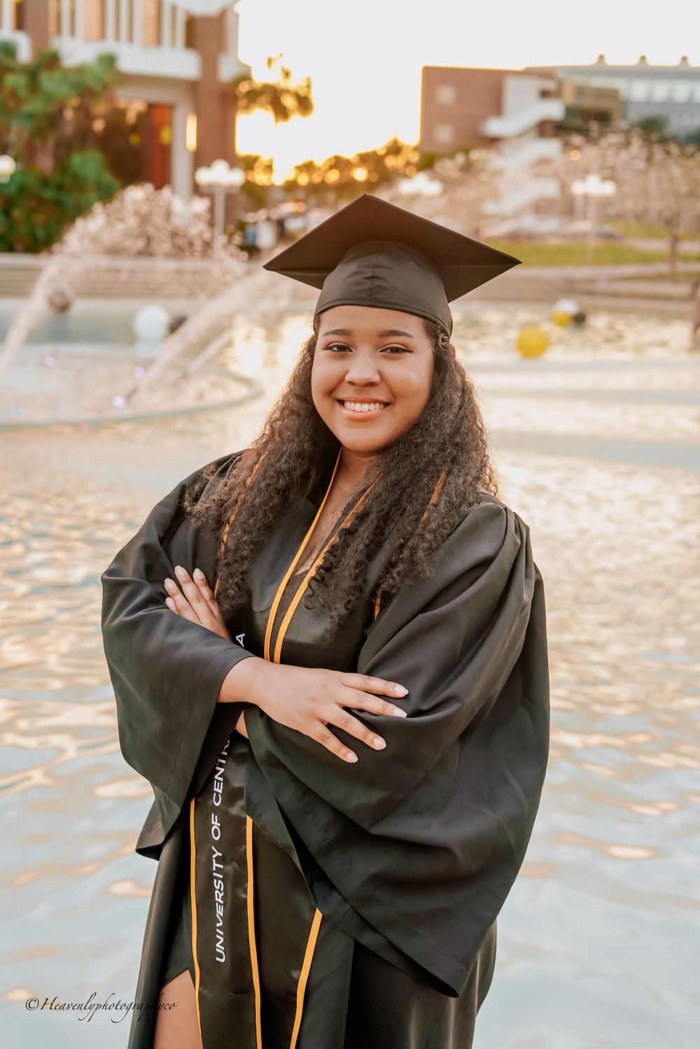 Graduate in black cap and gown smiles brightly during outdoor graduation photoshoot.