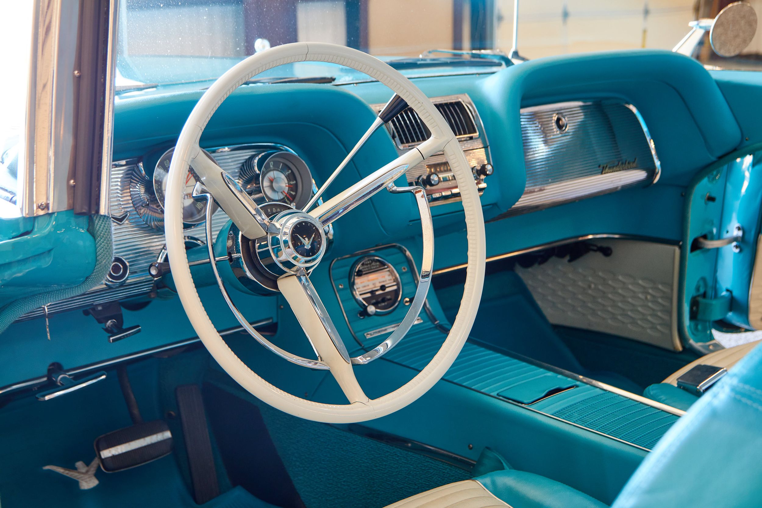 Vintage turquoise car interior with classic white steering wheel and dashboard.