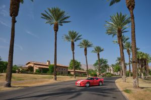 Red sports car driving down a palm tree-lined street in a luxurious neighborhood.