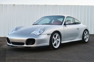 Silver Porsche 996 Carrera parked against white industrial wall.