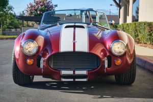 Front view of a burgundy Shelby Cobra replica with white racing stripes.
